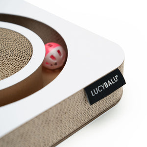 Nahaufnahme des LucyBalu Playbook Kratzbretts aus Wellpappe mit weißem Rahmen, sichtbarer Kratzfläche und integriertem rosa Spielball im Inneren.